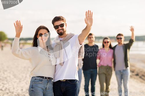 Image of happy couple with friends waving hands on beach