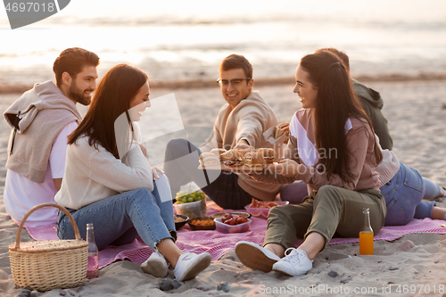 Image of happy friends eating sandwiches at picnic on beach