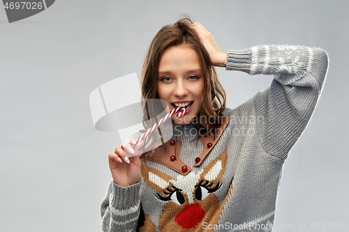 Image of woman in christmas sweater eating candy cane