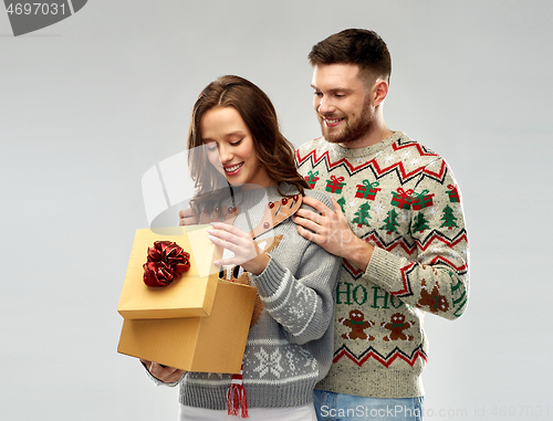 Image of happy couple in christmas sweaters with gift box