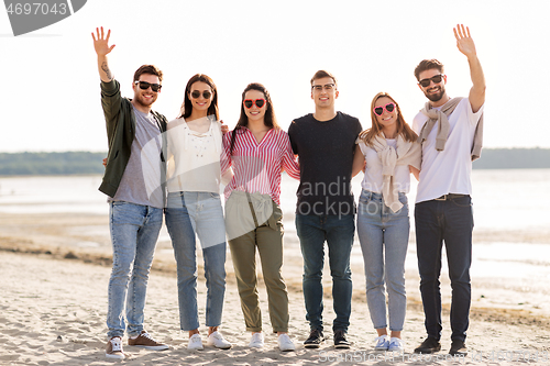 Image of happy friends waving hands on beach in summer