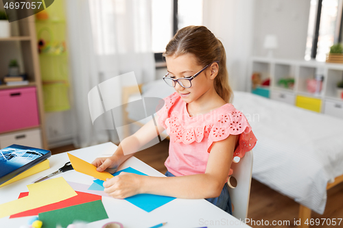 Image of girl with color paper sitting at table at home