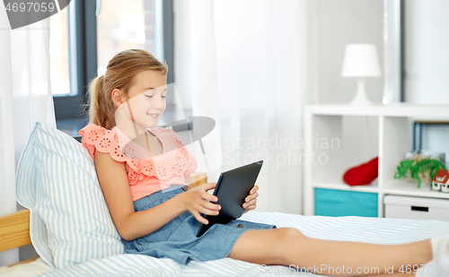 Image of smiling girl with tablet pc sitting on bed at home