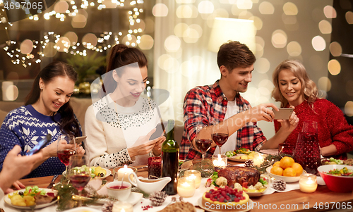 Image of friends with smartphones having christmas dinner