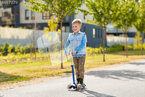 Image of happy little boy riding scooter in city