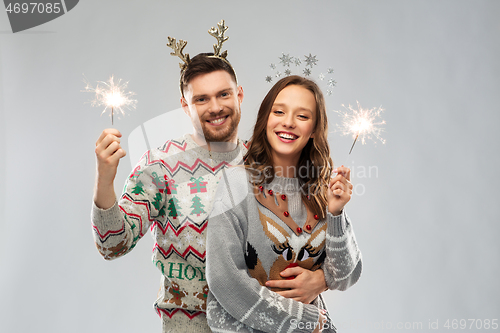 Image of happy couple in christmas sweaters with sparklers