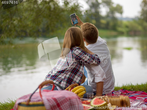 Image of Couple taking a selfie by mobile phone while enjoying picnic tim