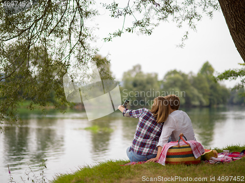 Image of Couple taking a selfie by mobile phone while enjoying picnic tim