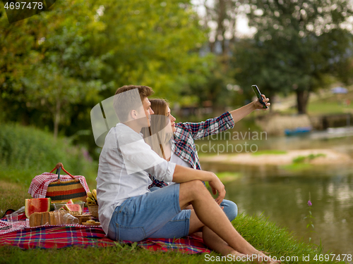 Image of Couple taking a selfie by mobile phone while enjoying picnic tim