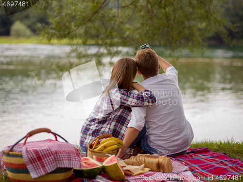 Image of Couple taking a selfie by mobile phone while enjoying picnic tim