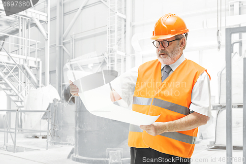 Image of The builder in orange helmet against industrial background