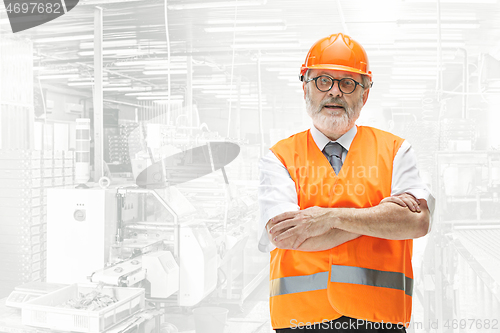 Image of Professional senior builder in orange helmet against industrial background