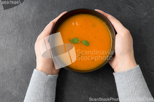 Image of hands with bowl of pumpkin cream soup on table