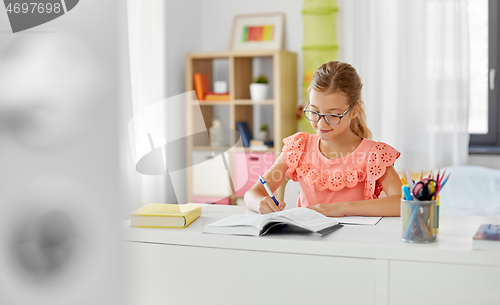 Image of student girl with book writing to notebook at home