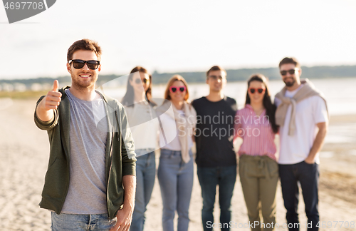 Image of happy man with friends on beach showing thumbs up