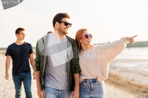 Image of happy friends walking along summer beach