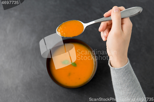 Image of hands with bowl of pumpkin cream soup on table