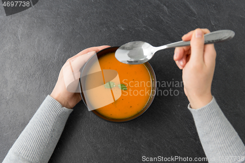 Image of hands with bowl of pumpkin cream soup on table