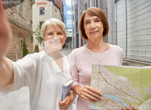 Image of senior women with map and city guide taking selfie