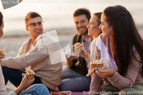 Image of happy friends eating sandwiches at picnic on beach