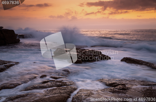 Image of Coastal sunrise waves crashing onto rocks