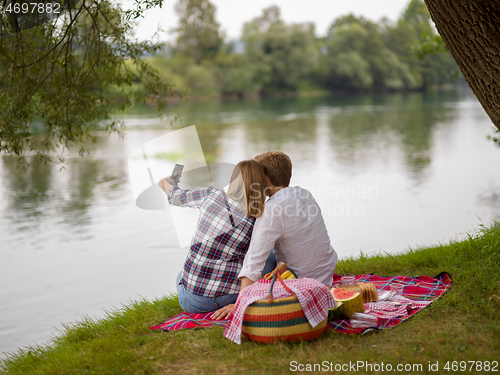 Image of Couple taking a selfie by mobile phone while enjoying picnic tim