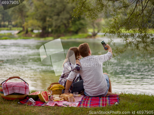 Image of Couple taking a selfie by mobile phone while enjoying picnic tim