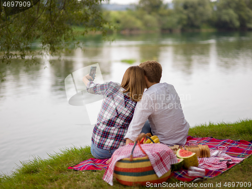 Image of Couple taking a selfie by mobile phone while enjoying picnic tim