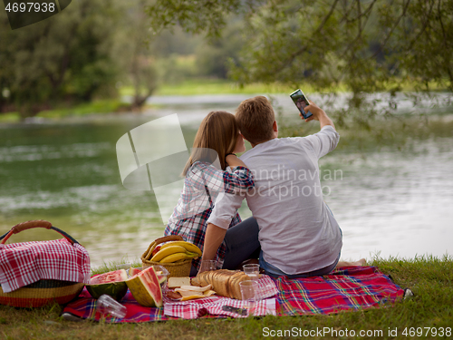 Image of Couple taking a selfie by mobile phone while enjoying picnic tim
