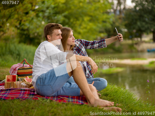 Image of Couple taking a selfie by mobile phone while enjoying picnic tim