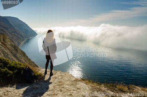 Image of A girl stands on a hill and observes an unusual phenomenon of nature over the sea