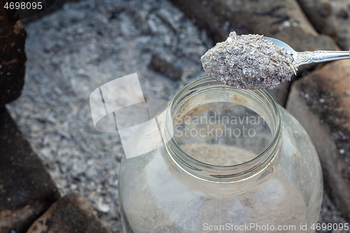 Image of Spoon pours fresh wood ash into a glass storage jar