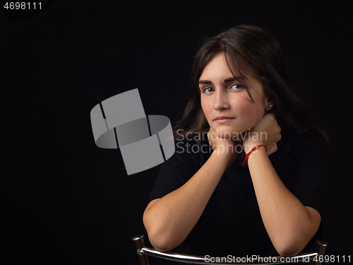 Image of Portrait of a young girl with her elbows on the back of a chair, the girl looks into the frame