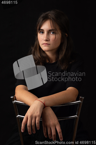 Image of Portrait of a young girl sitting on a high chair with her hands folded on the back of the chair