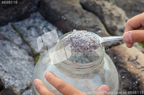 Image of Hands pouring fresh wood ash into a glass jar