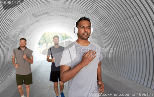 Image of male friends with headphones running outdoors