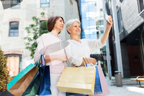 Image of old women with shopping bags taking selfie in city