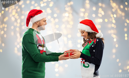 Image of happy couple in ugly sweaters with christmas gift