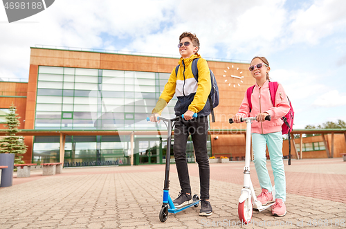 Image of happy school children with backpacks and scooters