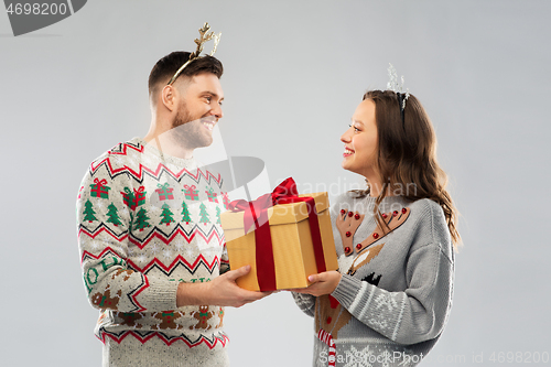 Image of happy couple in christmas sweaters with gift box