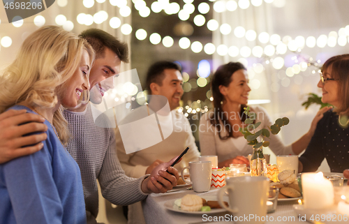 Image of happy couple with smartphone at family tea party