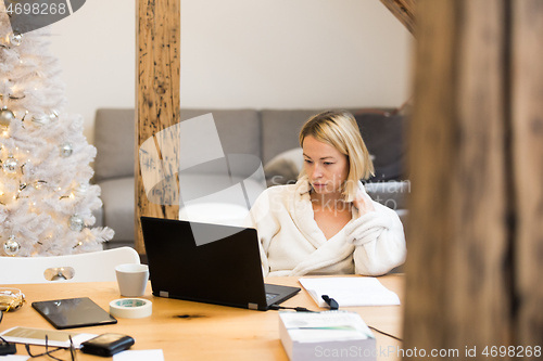 Image of Young female entrepreneur wearing cosy warm bathrobe working remotly from home in winter Christmas time during 2020 corona virus pandemic. Work from home, selter in place, concept.