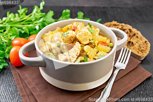 Image of Chicken with vegetables and peas in saucepan on dark board