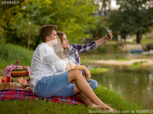 Image of Couple taking a selfie by mobile phone while enjoying picnic tim