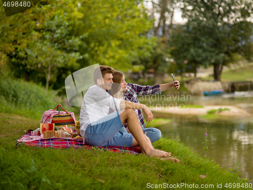 Image of Couple taking a selfie by mobile phone while enjoying picnic tim