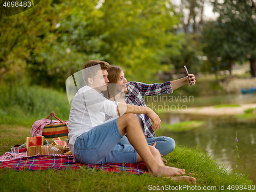 Image of Couple taking a selfie by mobile phone while enjoying picnic tim
