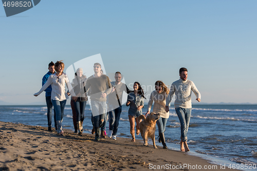 Image of Group of friends running on beach during autumn day