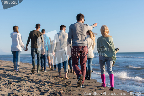 Image of Group of friends running on beach during autumn day