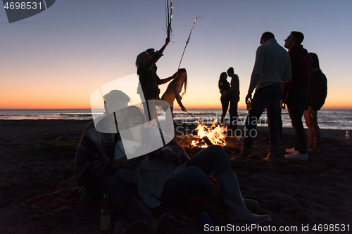 Image of Couple enjoying bonfire with friends on beach