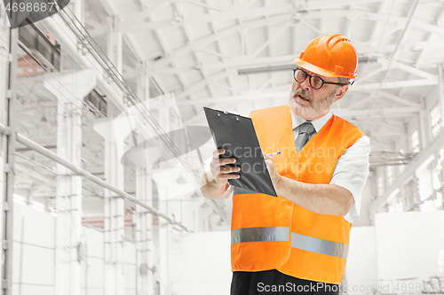 Image of Professional senior builder in orange helmet against industrial background